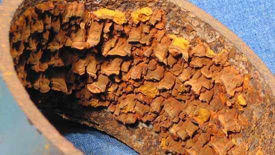 Close-up photograph of the inner wall of a pipe with multiple layers of rust peeling off.